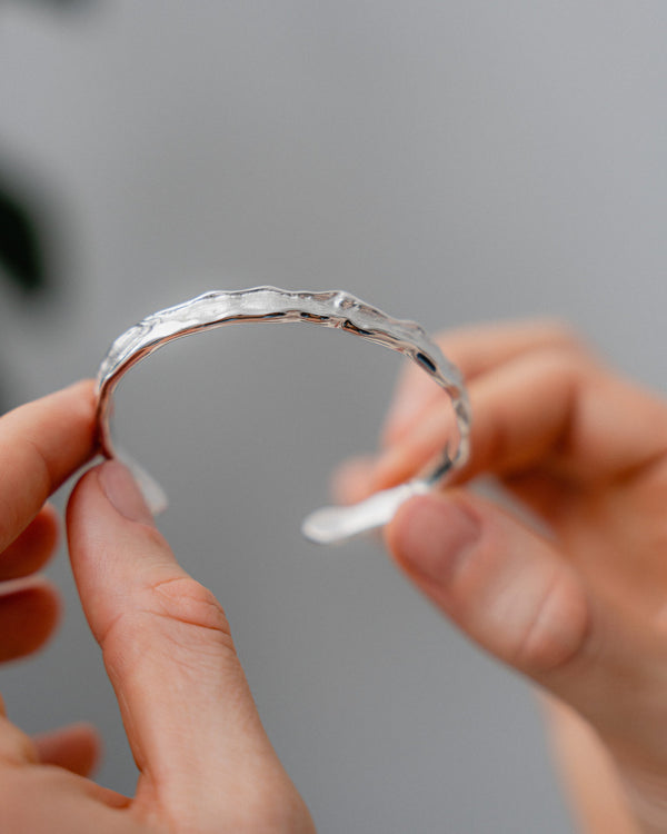 Die Detailaufnahme zeigt die intensive meteoritenaehnliche Raw Struktur des silbernen Armreifs die durch tief modellierte Linien elegante futuristische Tiefe erzeugt und der schmalen Form einen markanten modernen Charakter verleiht Sprezzi Fashion