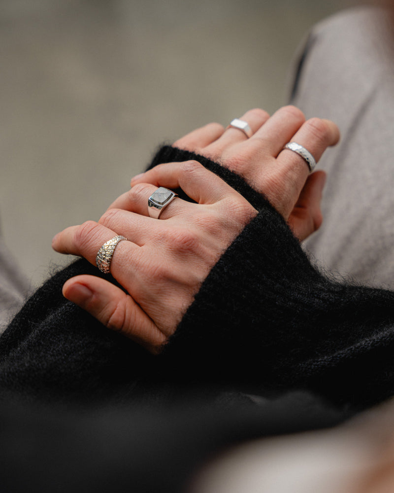 Der Balance Siegelring mit echtem Larvikit Stein zeigt die Kombination aus natürlicher Struktur und massivem 925 Silber am Finger eines Mannes mit weiteren edlen Ringen Sprezzi Fashion