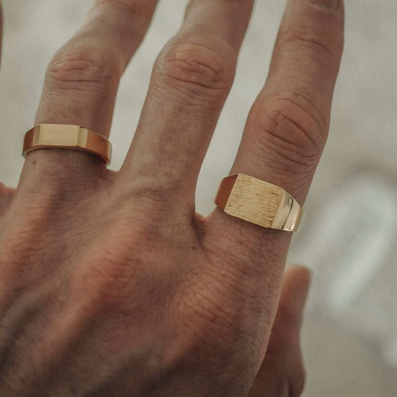 Die beiden goldenen Raw Ringe zeigen im getragenen Look ihre handgravierte Struktur deren warme Oberflaeche und eckige Form moderner Minimalismus und klare Praesenz verbinden wodurch ein markantes maennliches Set entsteht Sprezzi Fashion