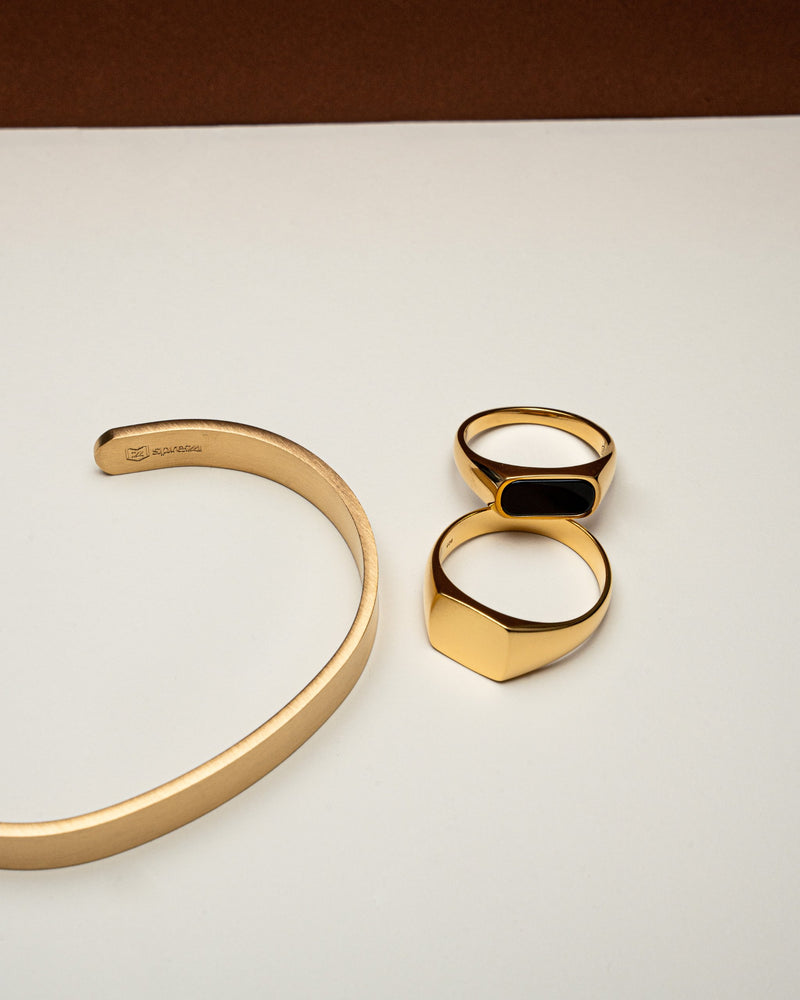 Zwei goldene Ringe liegen nebeneinander der Onyx Thin Ring mit schwarzem Inlay und der Silver Matt Ring mit matter Oberflaeche strahlen Luxus und Handarbeit aus Sprezzi Fashion