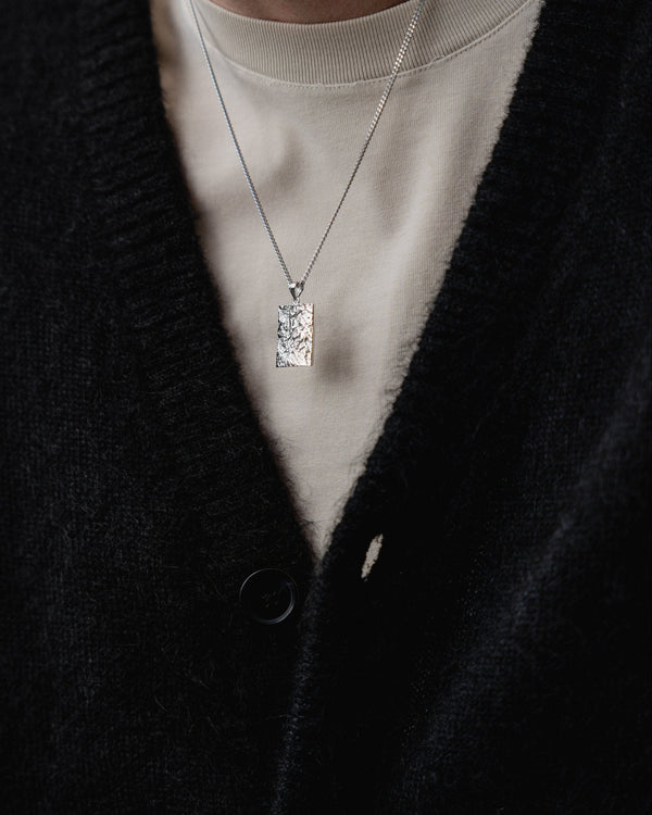 Getragen wirkt der eckige rhodinierte Anhaenger markant und zeigt meteoritenartige Struktur die modernen technischen Stil und maennliche Praesenz erzeugt Sprezzi Fashion