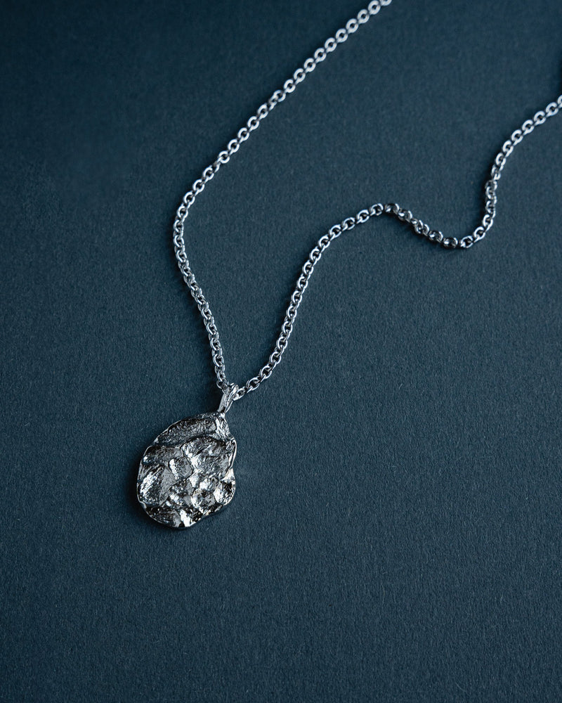 Die Halskette verbindet robustes 925 Silber mit einem futuristischen ovalen Anhaenger dessen meteoritenartige modellierte Struktur und rhodiniertes Finish moderne Tiefe kraftvollen Ausdruck und klare maennliche Eleganz zu einem praegenden Accessoire vereinen Sprezzi Fashion