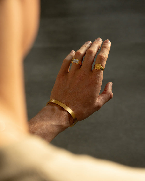 Herren Schmuck Set in Goldoptik mit zwei vergoldeten Siegelringen aus 925 Sterling Silber mit blauem Achat Naturstein und Kompass Gravur kombiniert mit modernem Edelstahl Armreif getragen an der Hand fuer einen kraftvollen maskulinen Look mit Symbolik und klarer Eleganz Sprezzi Fashion