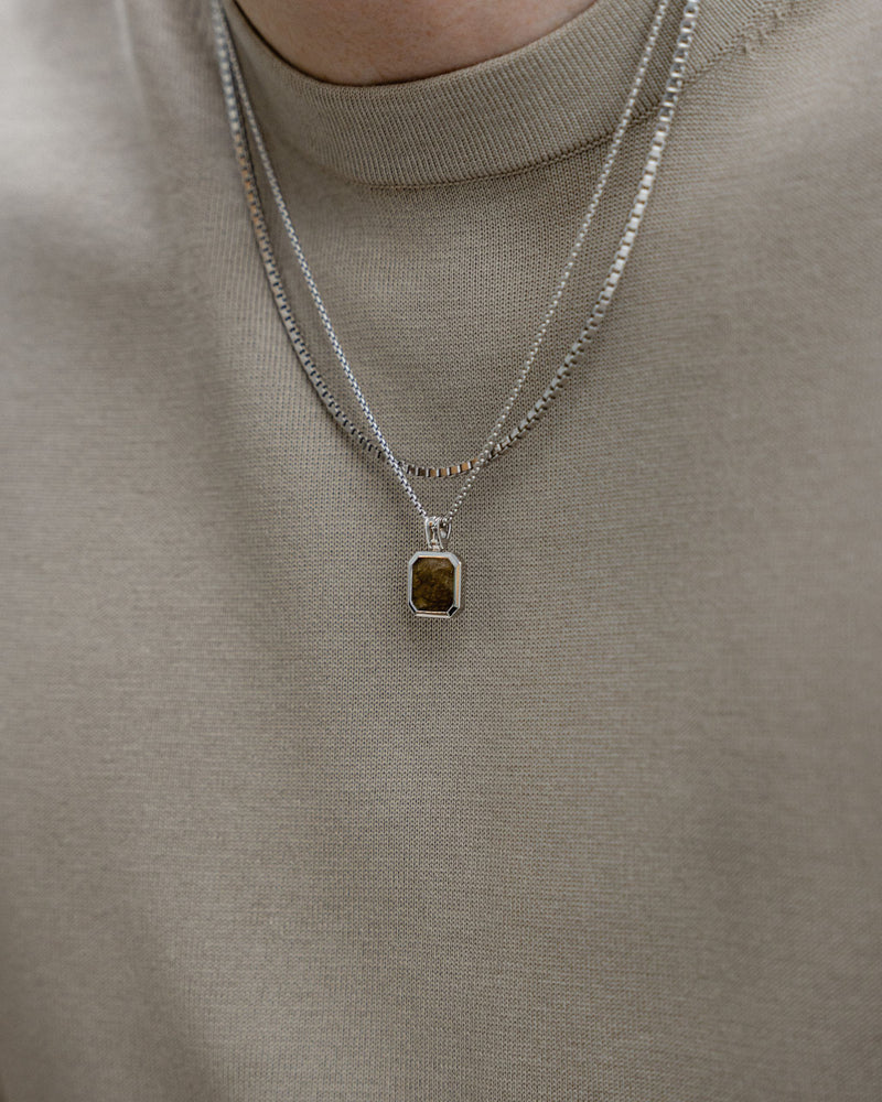 Ein Mann traegt zwei Halsketten aus 925 Sterling Silber eine mit Larvikit Stein und eine mit markanter Boxes XL Struktur das Zusammenspiel aus Glanz und Form zeigt moderne Eleganz Sprezzi Fashion