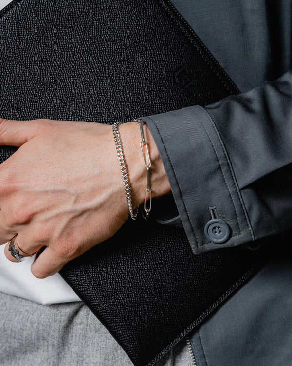 Ein Mann traegt zwei Armbänder aus 925 Sterling Silber Curb und Paperclip Design die Kombination aus Struktur und Glanz steht fuer modernen maskulinen Stil Sprezzi Fashion