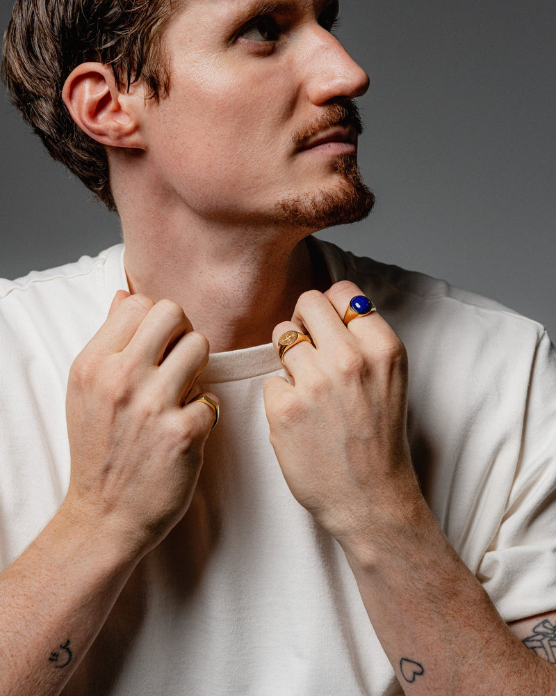 Ein Mann traegt den goldenen Lapislazuli Ring und den Kompassrose Ring beide gefertigt aus 925 Silber mit 18k Vergoldung der blaue Stein und die Gravur strahlen Stil Sprezzi Fashion