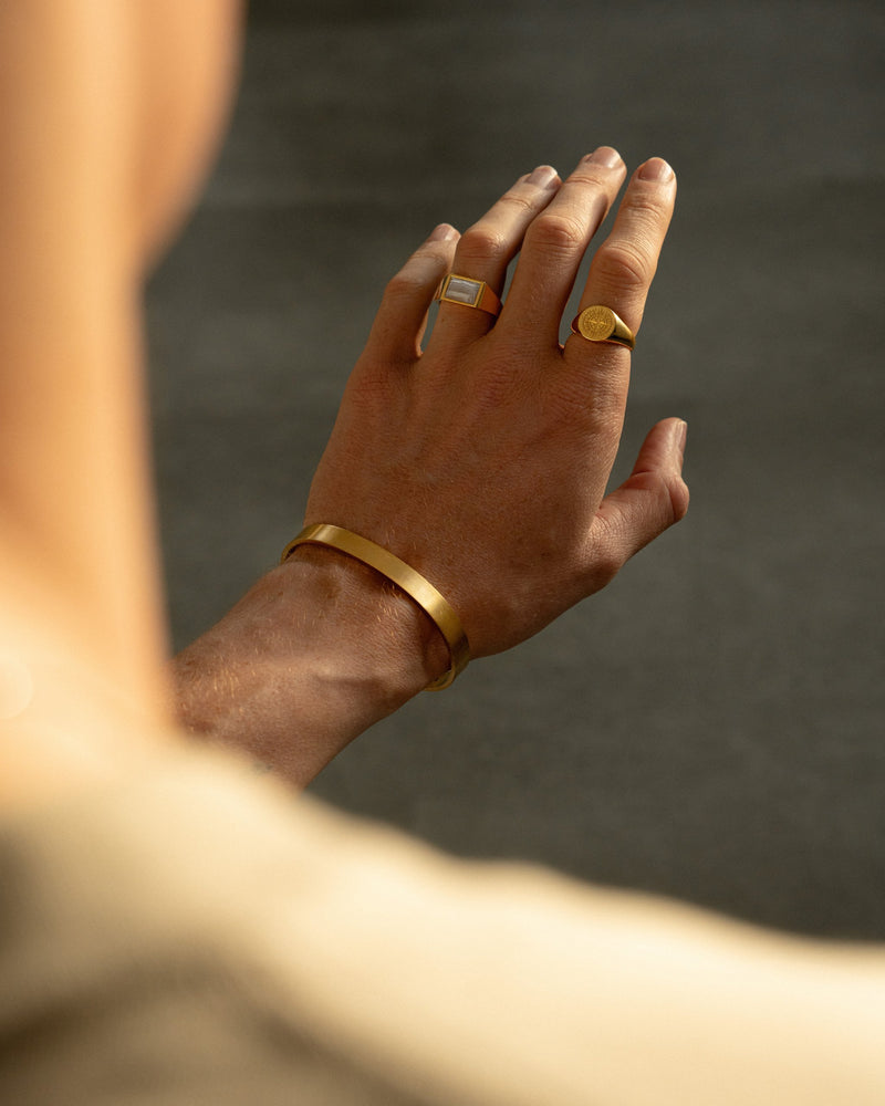 Ein Mann traegt den goldenen Kompassrose Ring den blauen Achat Ring und den gebuersteten Armreif die Kombination aus Symbolik Farbe und Textur strahlt Luxus Sprezzi Fashion