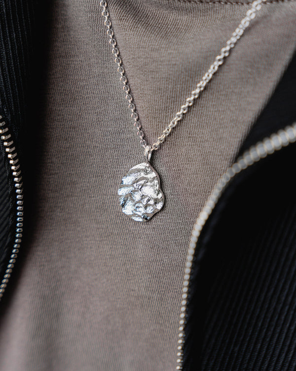 Die Nahaufnahme zeigt die meteoritenartige modellierte Oberflaeche die dem ovalen rhodinierten Anhaenger aus 925 Silber moderne technische Tiefe und markanten futuristischen Ausdruck verleiht Sprezzi Fashion