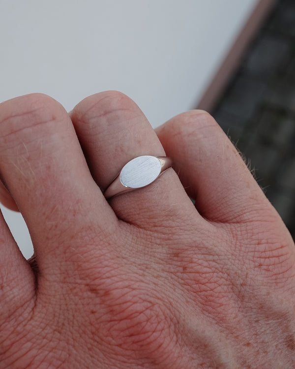 Der am Finger getragene Herrenring aus poliertem 925 Sterling Silber zeigt seine fein strukturierte Raw Oberfläche und ergänzt einen modernen reduzierten Stil mit zeitlos eleganter Ausstrahlung Sprezzi Fashion