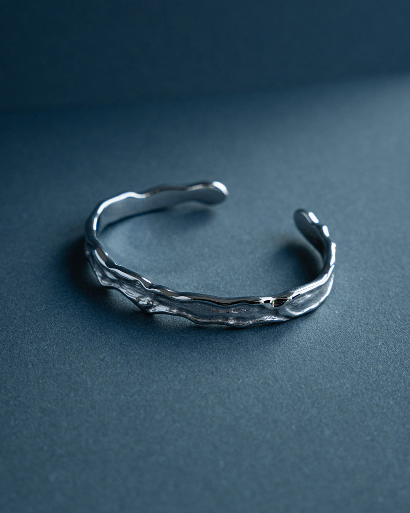 Zu sehen ist ein schmaler Armreif dessen Raw Struktur an aufgebrochene Metallflaechen erinnert und zusammen mit der offenen Form eine moderne technische Aesthetik erzeugt die markante maennliche Ausstrahlung und hochwertige Verarbeitung vereint Sprezzi Fashion