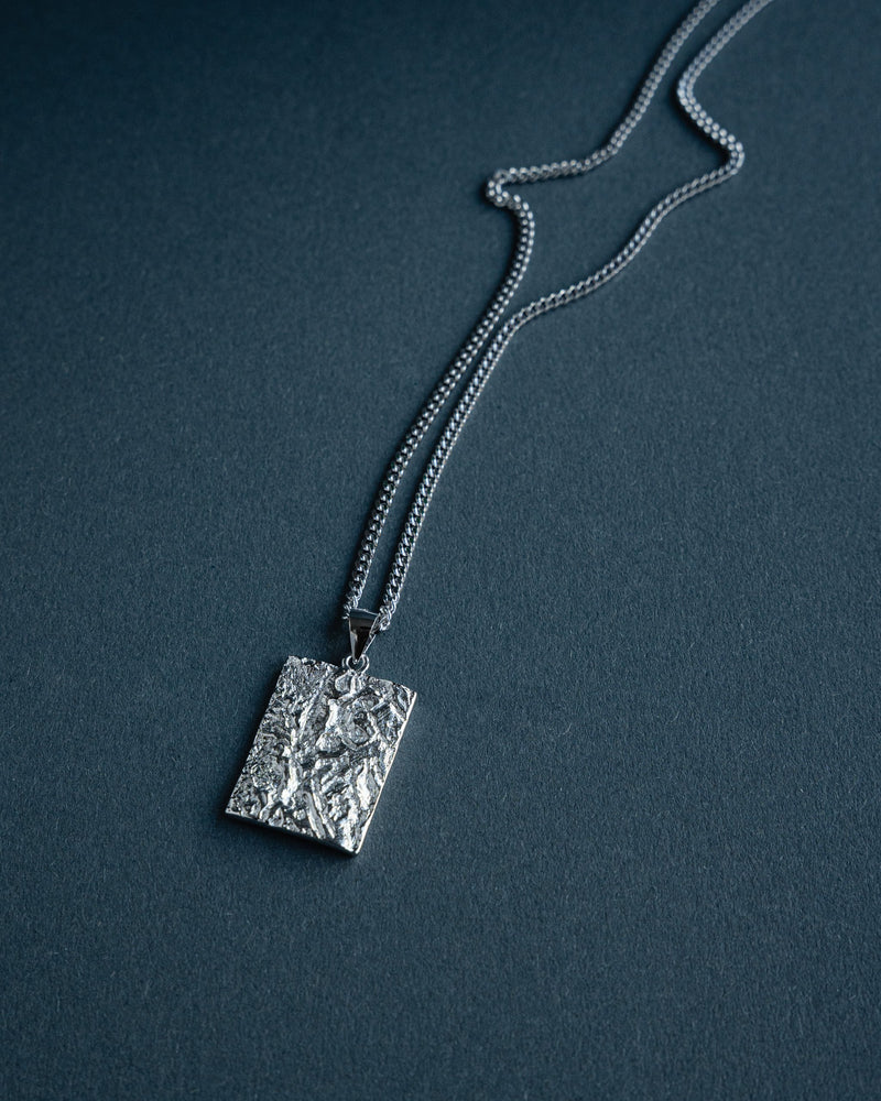 Zu sehen ist eine futuristisch gestaltete Halskette aus 925 Silber deren eckiger Anhaenger mit rhodinierter meteoriteninspirierter Oberflaeche praegende Tiefe und moderne technische Aesthetik erzeugt waehrend die klare Form maennliche Eleganz vermittelt Sprezzi Fashion