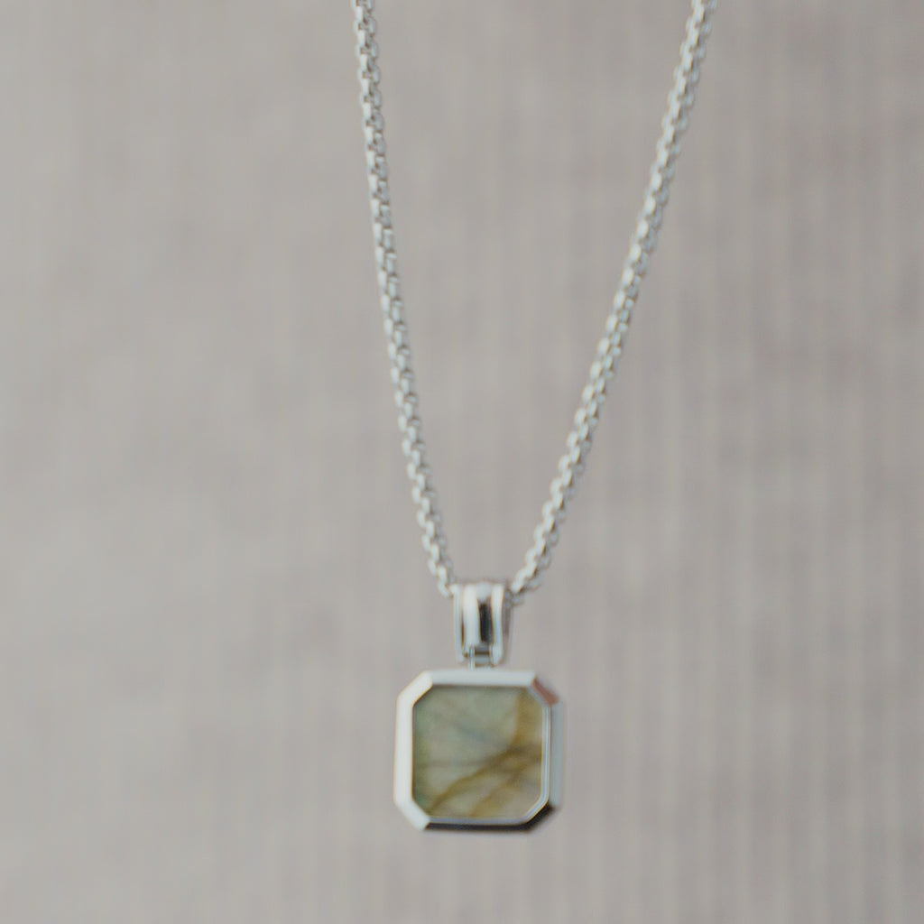 Nahaufnahme einer Herren Halskette aus 925 Sterling Silber mit eckigem Larvikit Stein Anhänger in Grau, dessen natürliche Maserung und feine Farbnuancen durch das Licht dezent hervorgehoben werden Sprezzi Fashion