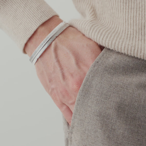 Nahaufnahme eines Herren Armreifs aus 925 Sterling Silber im Feder Design, getragen am Handgelenk, wobei die feinen Linien der Struktur das Licht dezent reflektieren Sprezzi Fashion