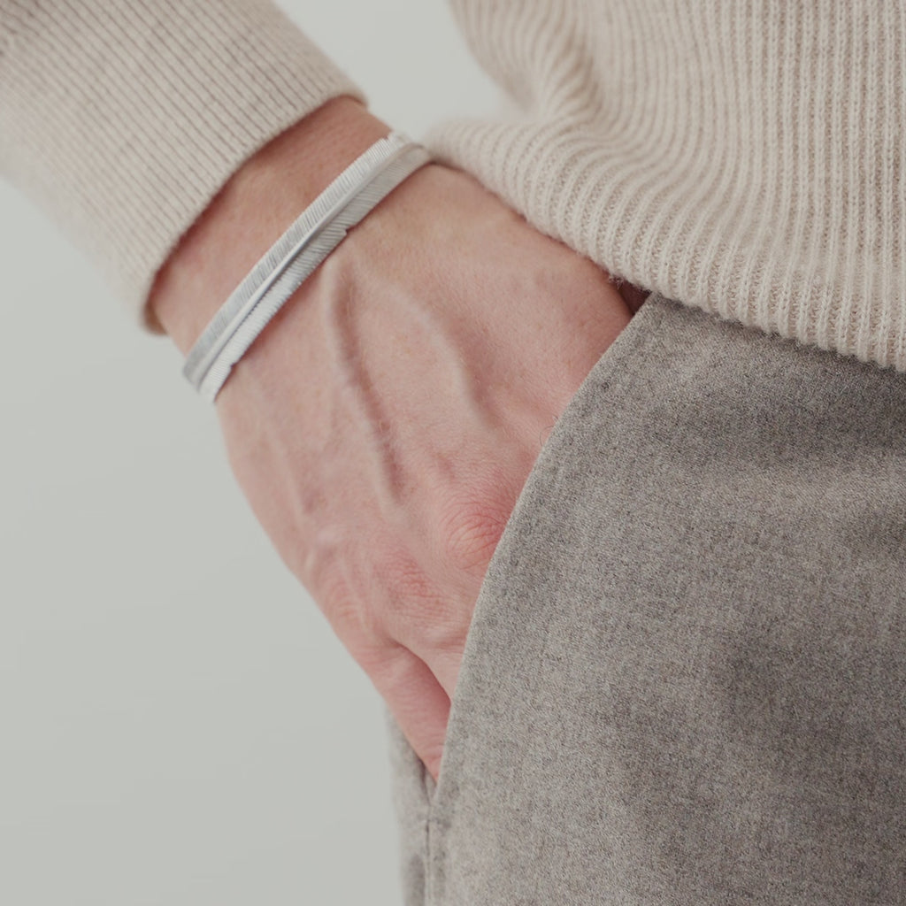 Nahaufnahme eines Herren Armreifs aus 925 Sterling Silber im Feder Design, getragen am Handgelenk, wobei die feinen Linien der Struktur das Licht dezent reflektieren Sprezzi Fashion