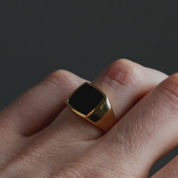 Detailansicht eines Siegelrings aus vergoldetem Silber mit schwarzem Onyx Stein in eckiger Form, bei dem die polierte Oberfläche des Rings das Licht reflektiert Sprezzi Fashion