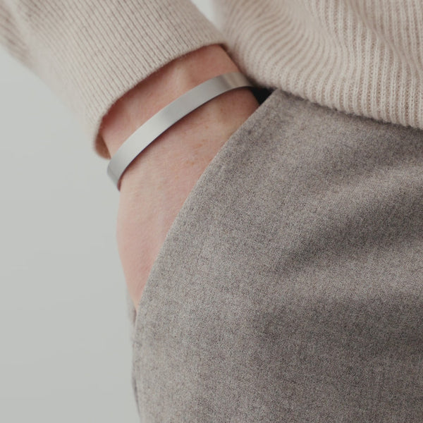 Der silberne Armreif aus gebürstetem Edelstahl zeigt eine dezente Lichtreflexion und ergänzt das Outfit durch seine minimalistische und hochwertige Erscheinung Sprezzi Fashion