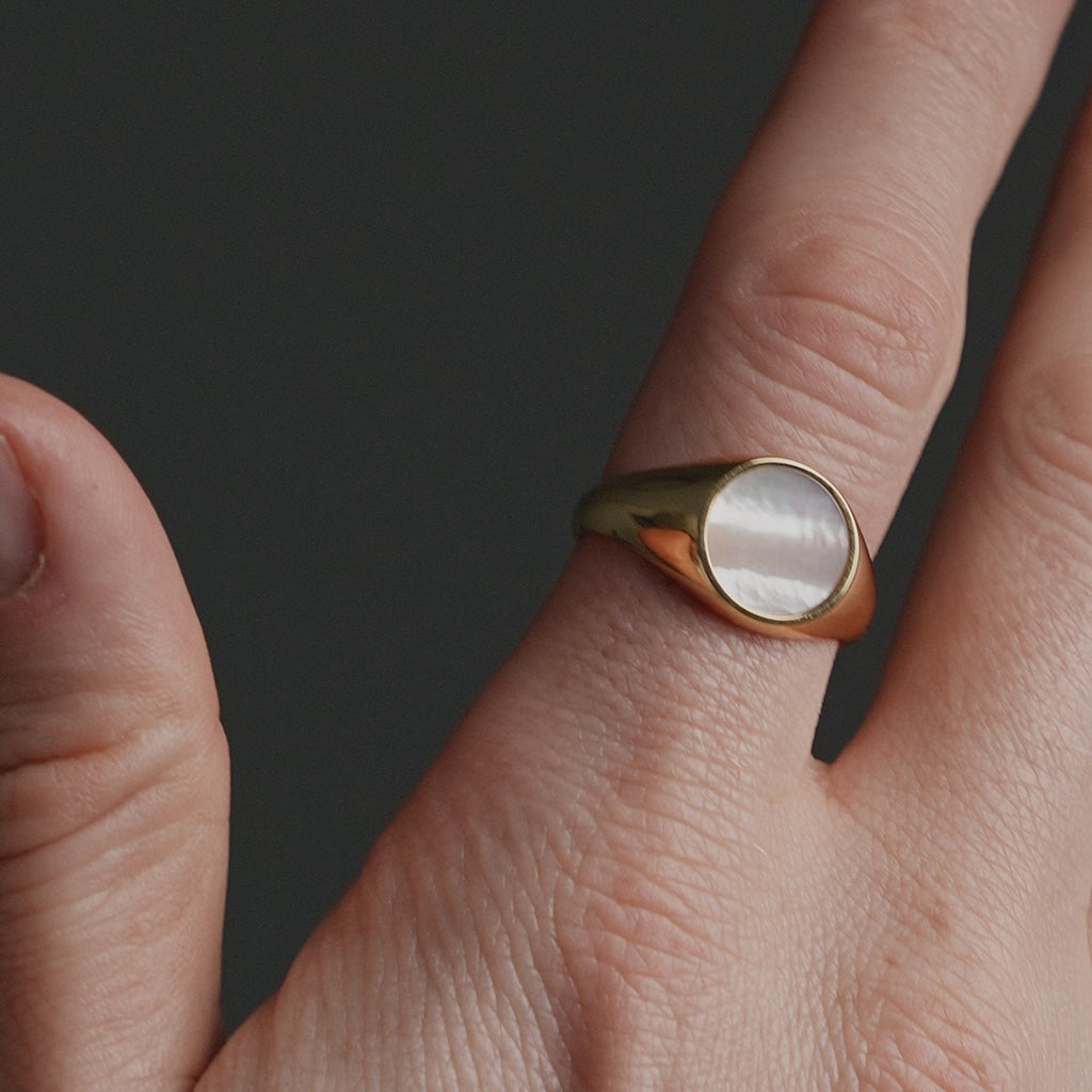 Detailansicht eines Siegelrings aus vergoldetem Silber mit rundem Perlmutt Stein, dessen glatte Oberfläche das Licht sanft reflektiert Sprezzi Fashion