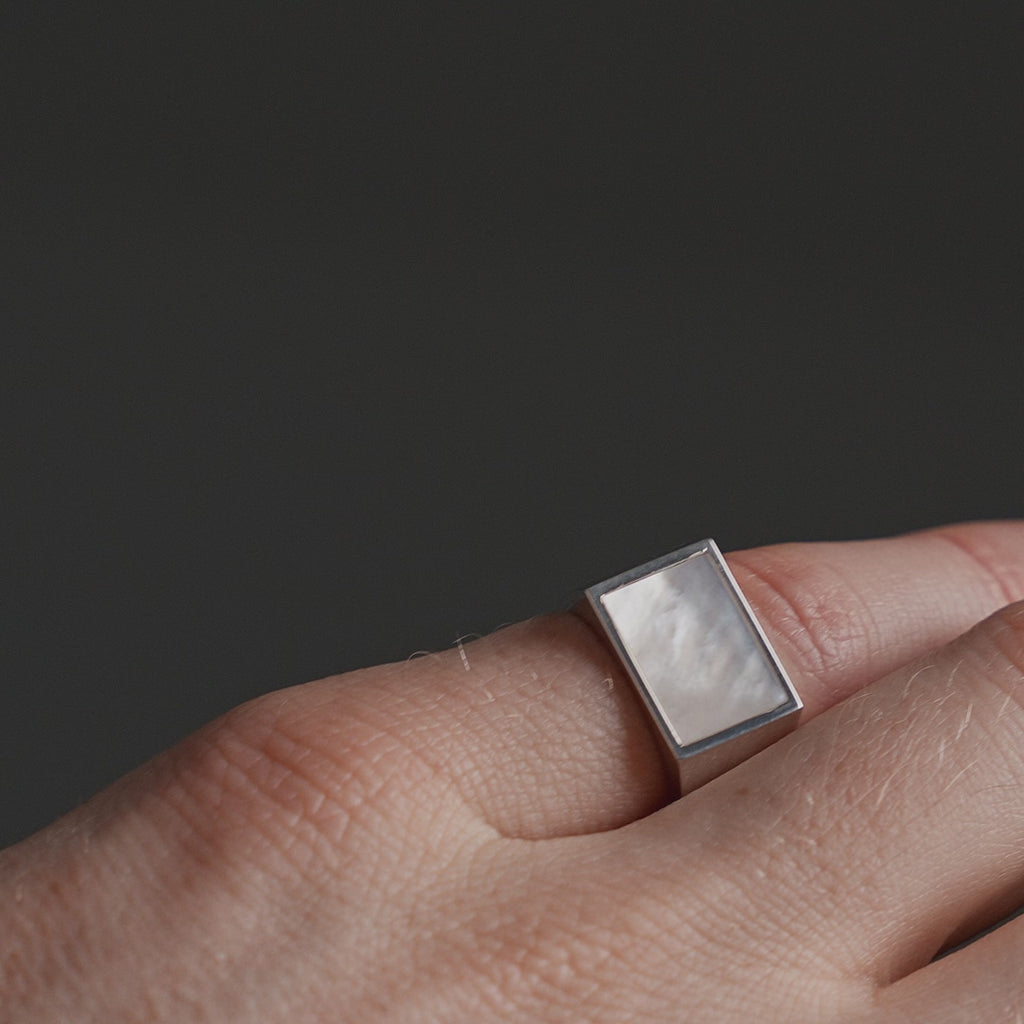 Detailansicht eines Siegelrings aus 925 Silber mit hellem Perlmutt Stein in eckiger Form, dessen glatte Oberfläche das Licht sanft reflektiert Sprezzi Fashion