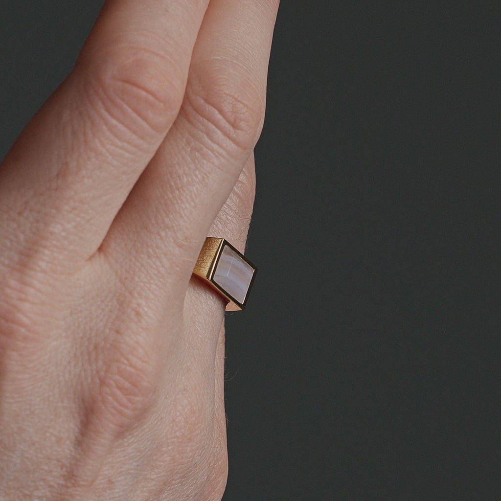 Nahaufnahme eines goldenen Herren Siegelrings mit eckigem blauem Achat Stein, dessen helle Farbnuancen und natürliche Struktur sanft im Licht schimmern Sprezzi Fashion