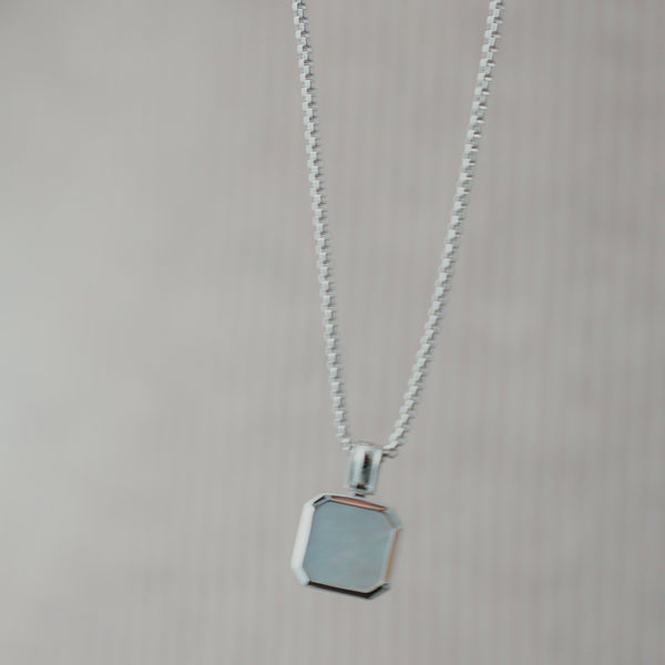 Nahaufnahme einer Herren Halskette aus 925 Sterling Silber mit eckigem weiß schimmerndem Perlmutt Anhänger, dessen Oberfläche das Licht weich reflektiert und je nach Blickwinkel unterschiedliche Nuancen zeigt Sprezzi Fashion
