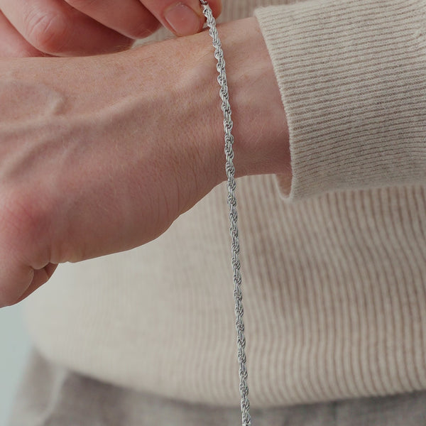 Nahaufnahme eines Herren Armbands aus 925 Sterling Silber im Rope Design, das locker am Handgelenk liegt und dessen gedrehte Glieder das Licht entlang der Struktur reflektieren Sprezzi Fashion